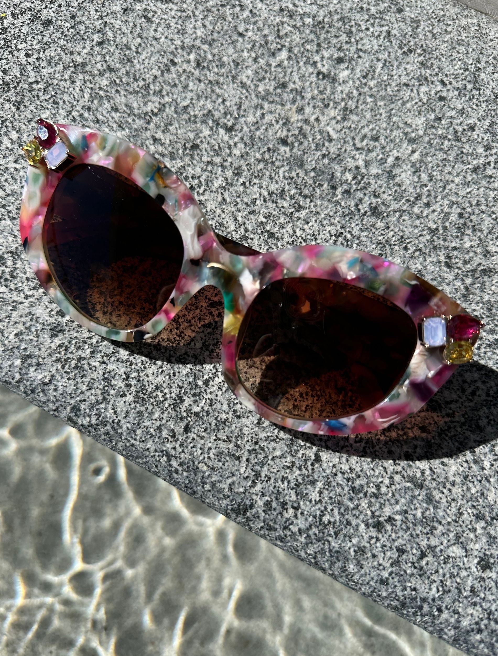 colourful framed sunglasses are placed on a textured stone ledge, highlighting their bright hues