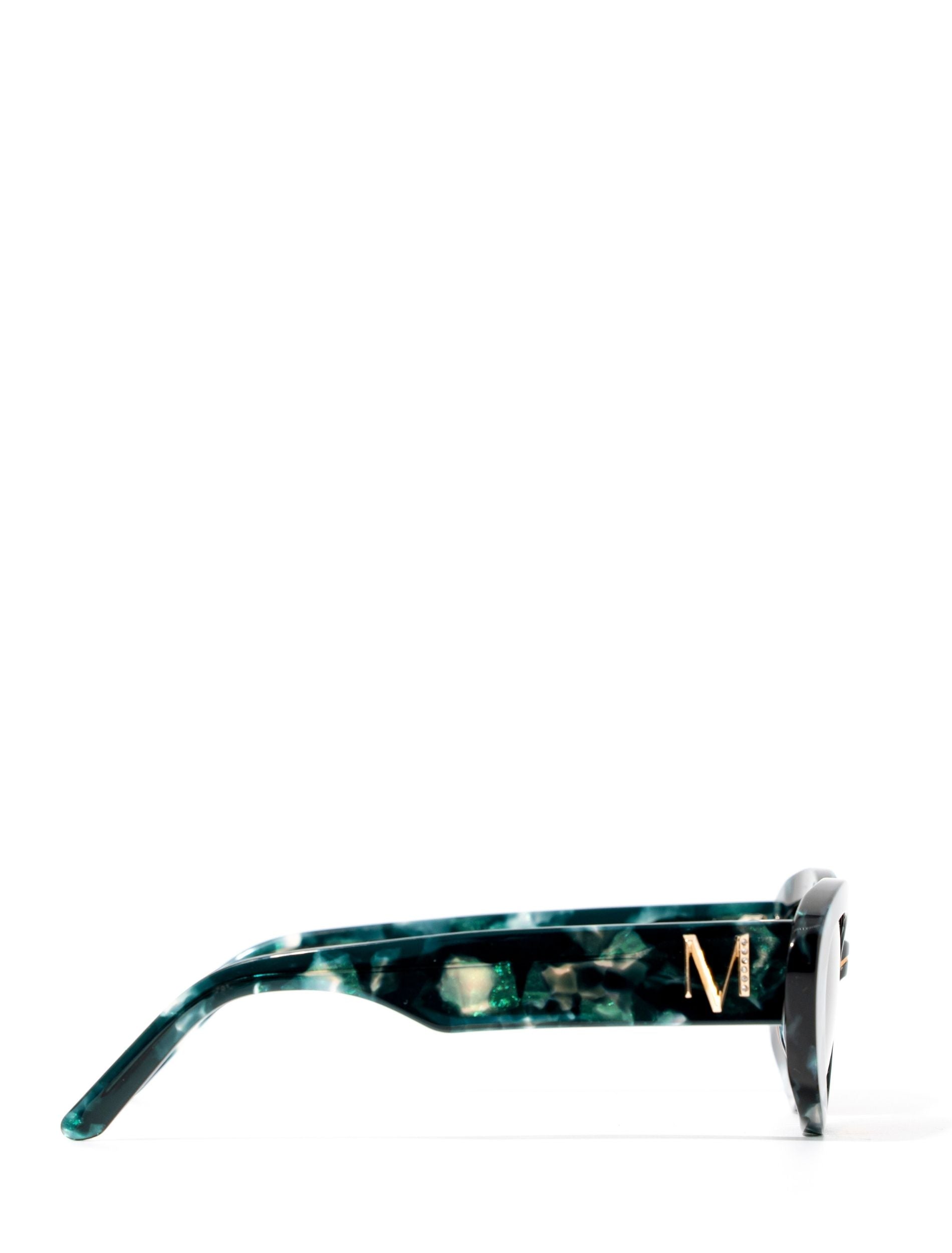 side view of a pair of stylish sunglasses in a green tortoise shell style displaced against a white back drop. You can see an embellished 'M' on the side of the frame arm