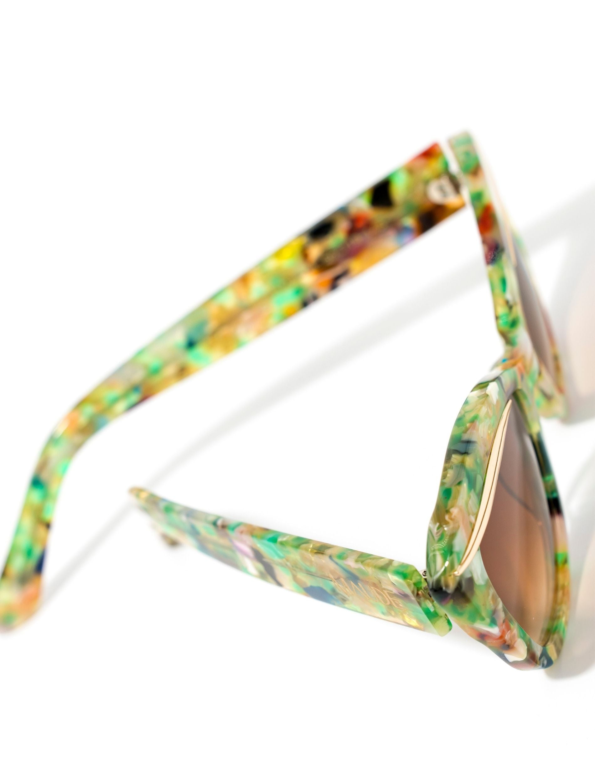 Colorful cat-eye sunglasses with a translucent multicolored frame and gradient brown lenses, featuring a stylish design and the brand name "MAUDE" on the side.