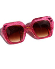 Pink glittery sunglasses with brown lenses on a white background