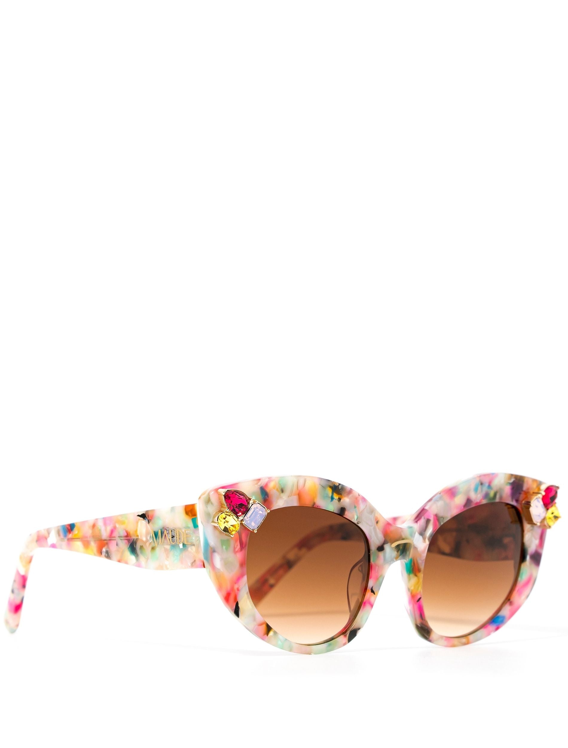 side view of multi-coloured cat-eye sunglasses with gradient brown lenses and gemstone embellishments on the frame corners, set against a white background