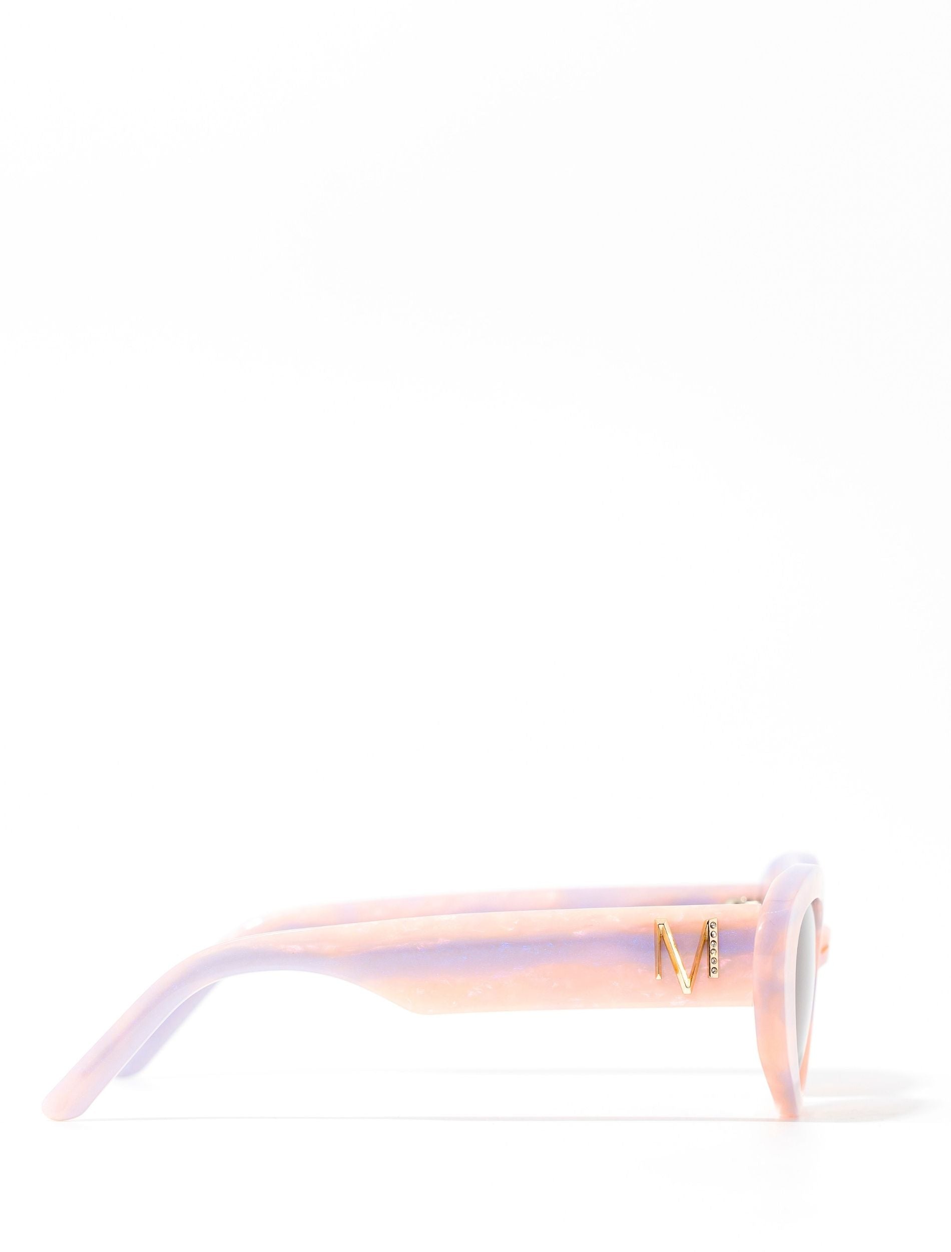 Side view of stylish pair of pastel pink and lilac sunglasses set against a white background. there is a gold 'M' on the arm of the frame.