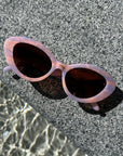 Top view of a pair of stylish pastel pink and lilac sunglasses, resting on a textured stone, highlighting their reflective frames and modern style