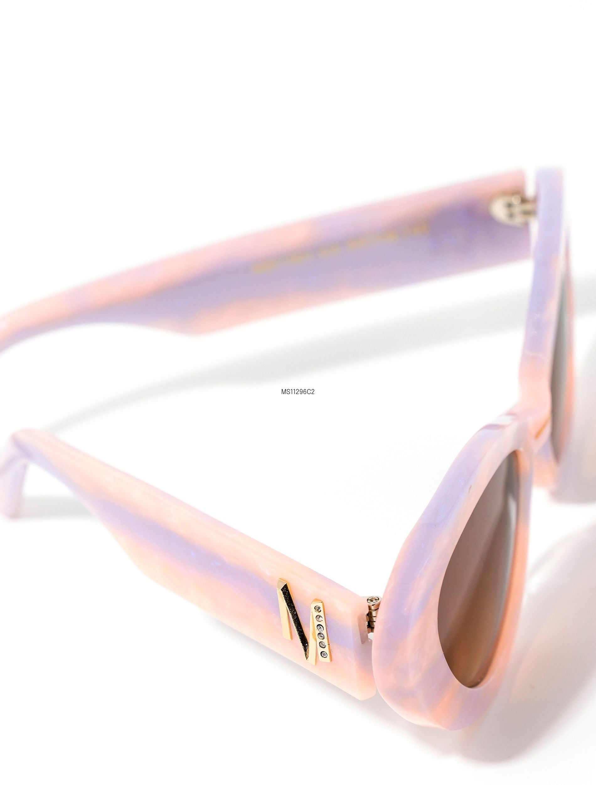 top view of stylish pair of pastel pink and lilac sunglasses with a brown gradient lense set against a white background. there is a gold &#39;M&#39; on the arm of the frame.