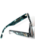 top view of a pair of stylish sunglasses in a green tortoise shell style displaced against a white back drop. the lenses are a gradient brown. You can see an embellished 'M' on the side of the frame arm