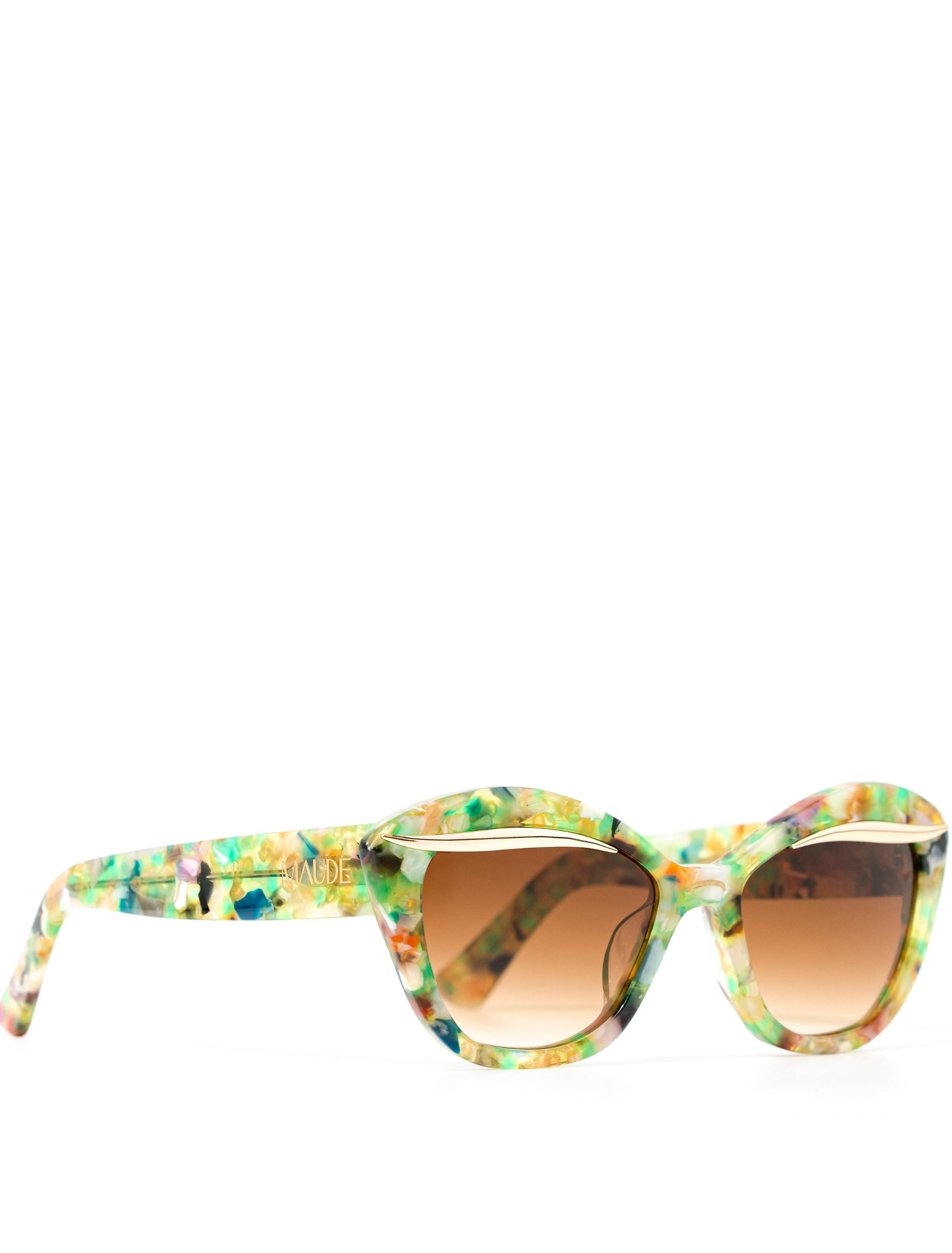 Colorful sunglasses with a translucent multicolored frame and gradient brown lenses, featuring a stylish design and the brand name "MAUDE" on the side.