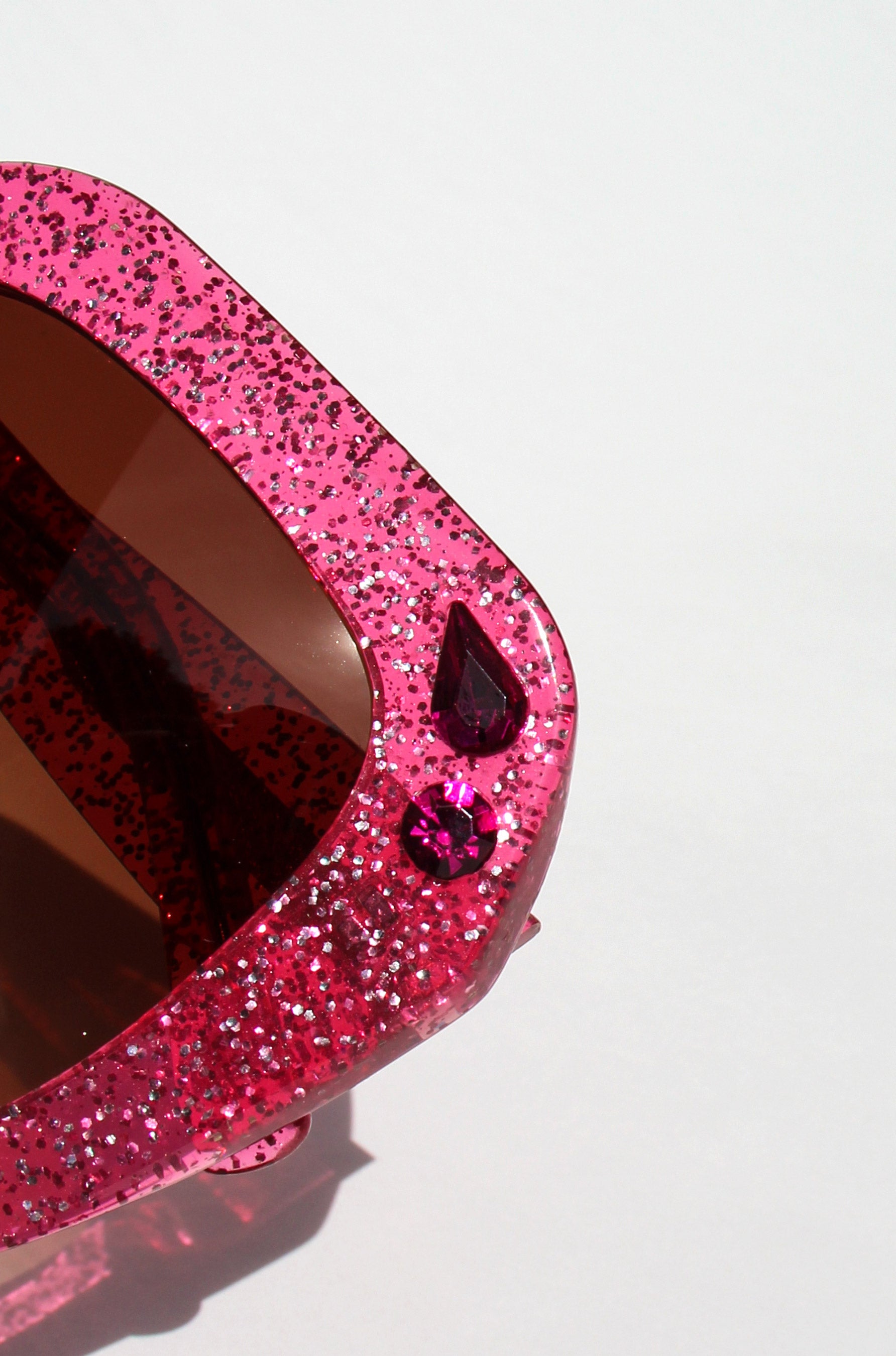 Pink glittery sunglasses with a gemstone on a white background