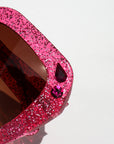 Pink glittery sunglasses with a gemstone on a white background