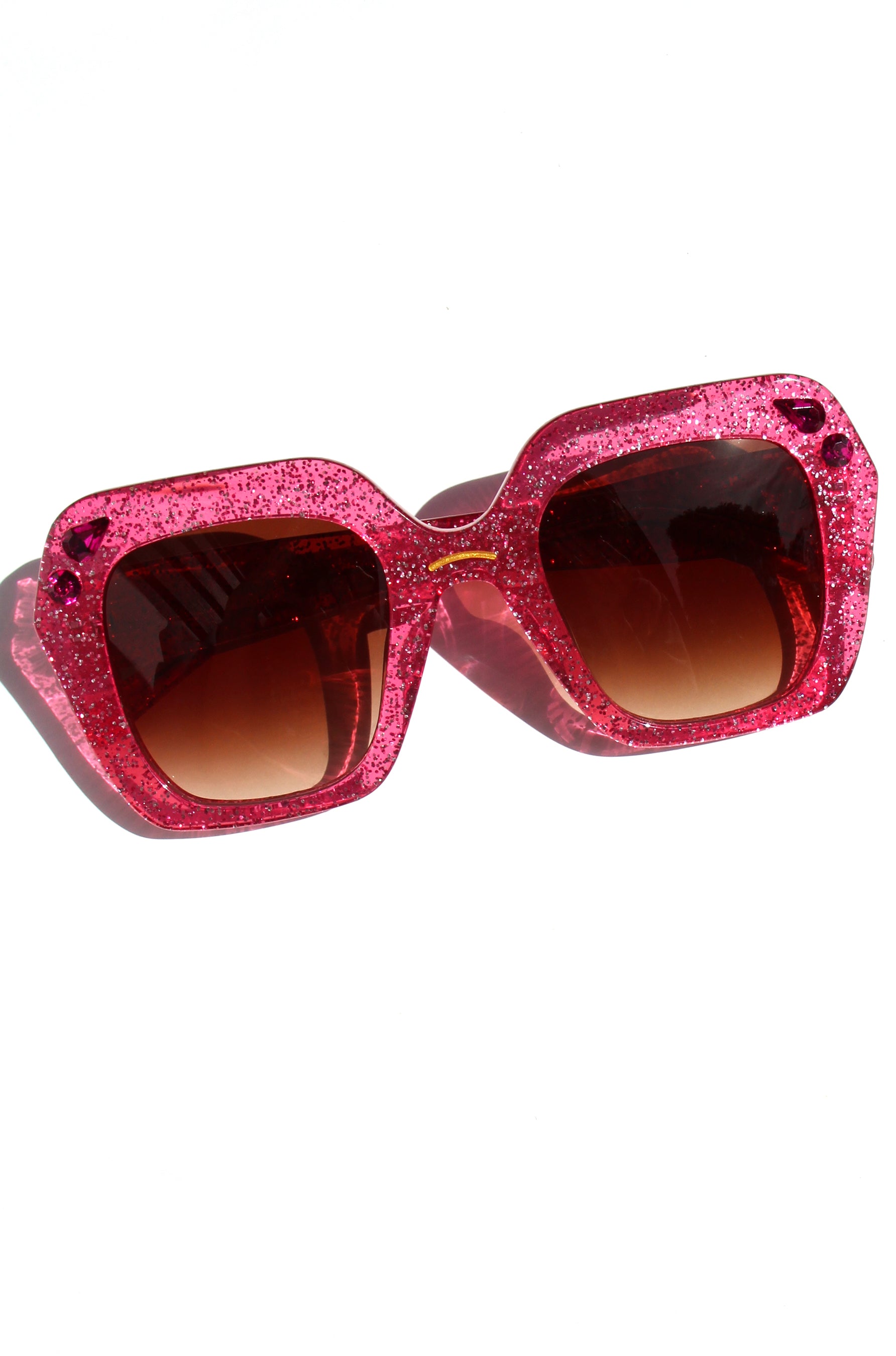 Pink glittery sunglasses with brown lenses on a white background