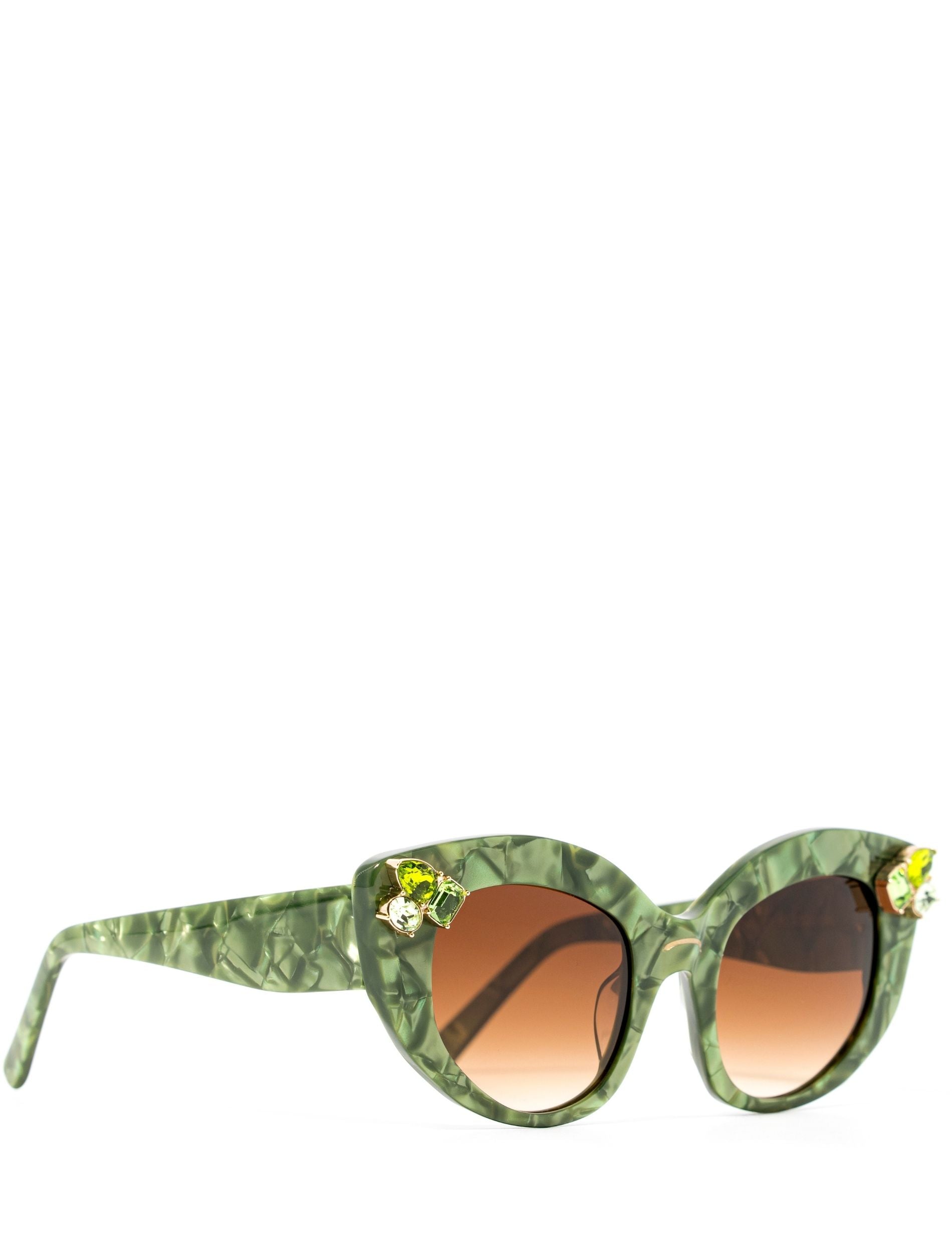 Side view of stunning cat eye sunglasses crafted with a green pearlescent look,  featuring gemstone embellishments on the upper corners of the frame and a brown gradient lense. Set against a white backdrop