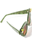 Top view of stunning cat eye sunglasses crafted with a green pearlescent look,  featuring gemstone embellishments on the upper corners of the frame and a brown gradient lense. Set against a white backdrop